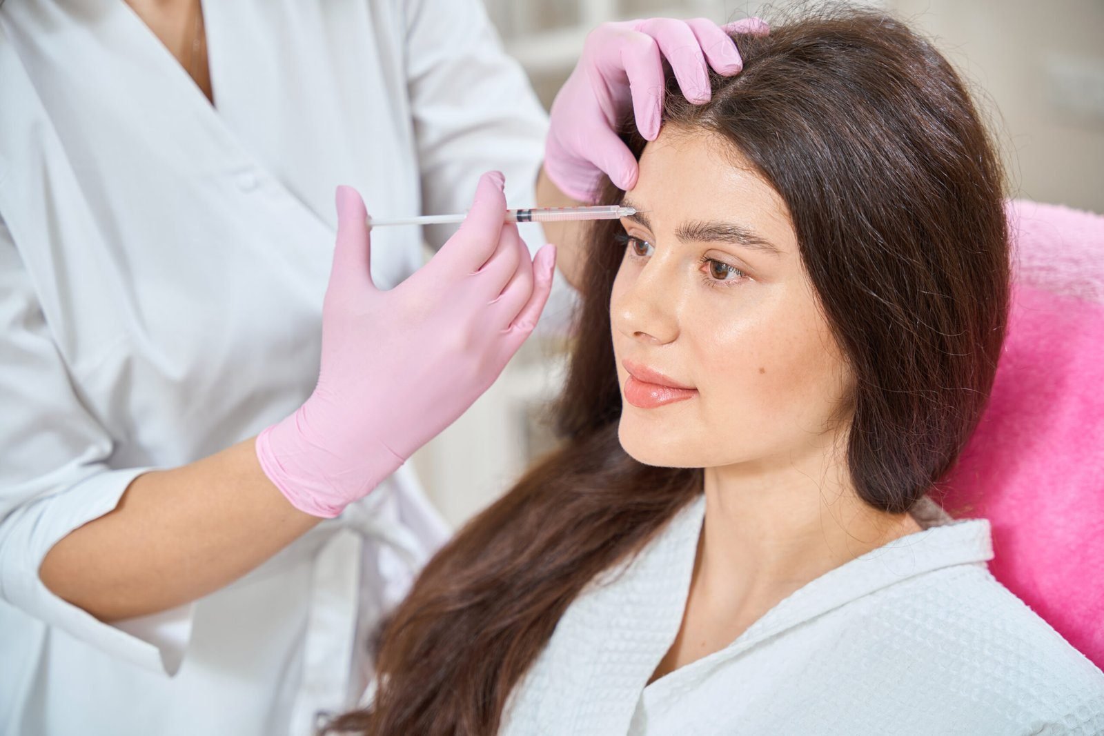 Woman receiving Botox injection on forehead from a professional wearing gloves.