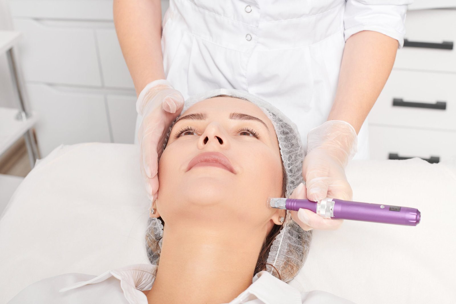 Woman receiving microneedling treatment on her cheek in a modern clinical spa by a professional in gloves.