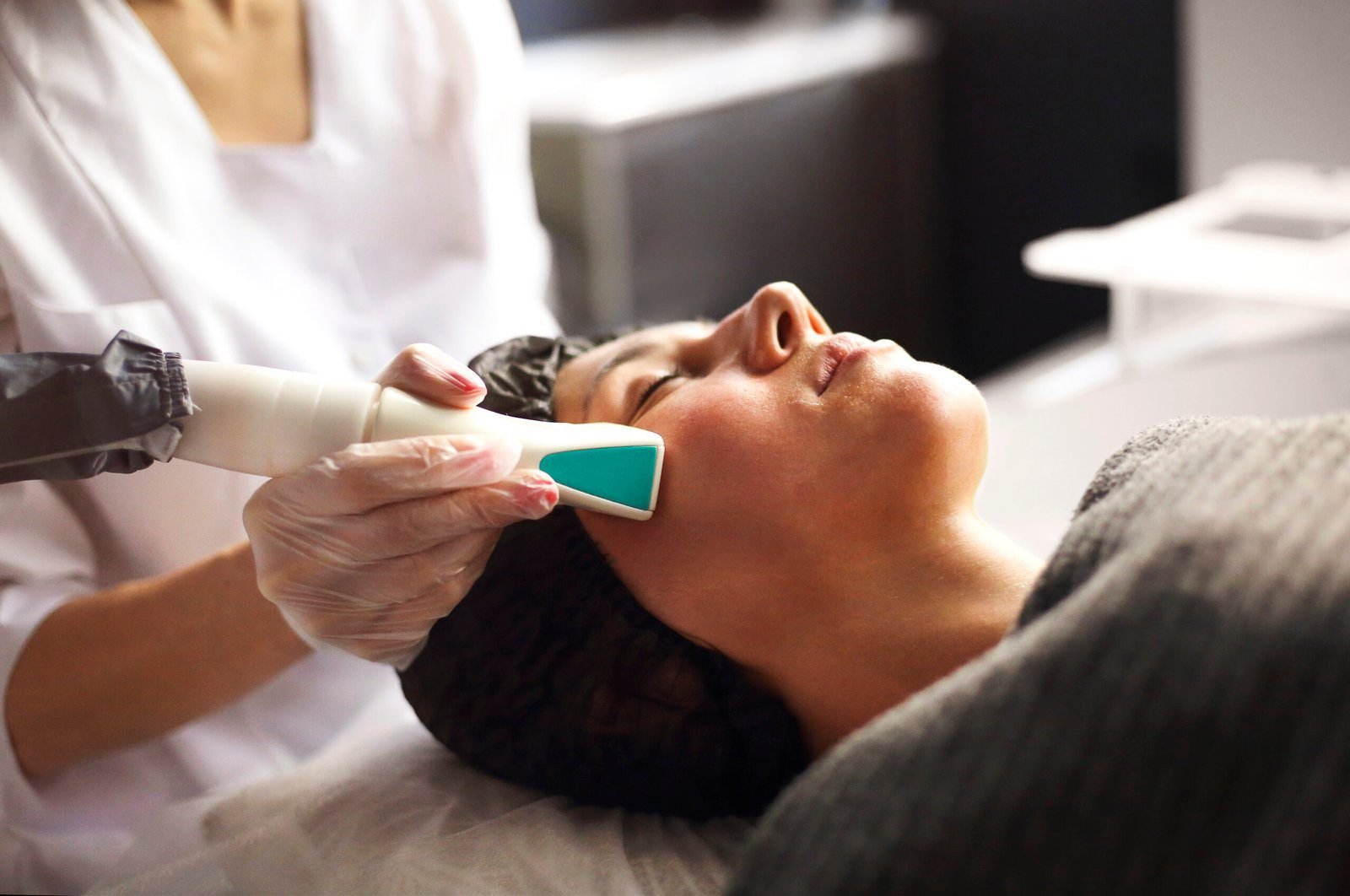 Woman receiving Ultherapy facial treatment by a professional in gloves at a clinical spa.